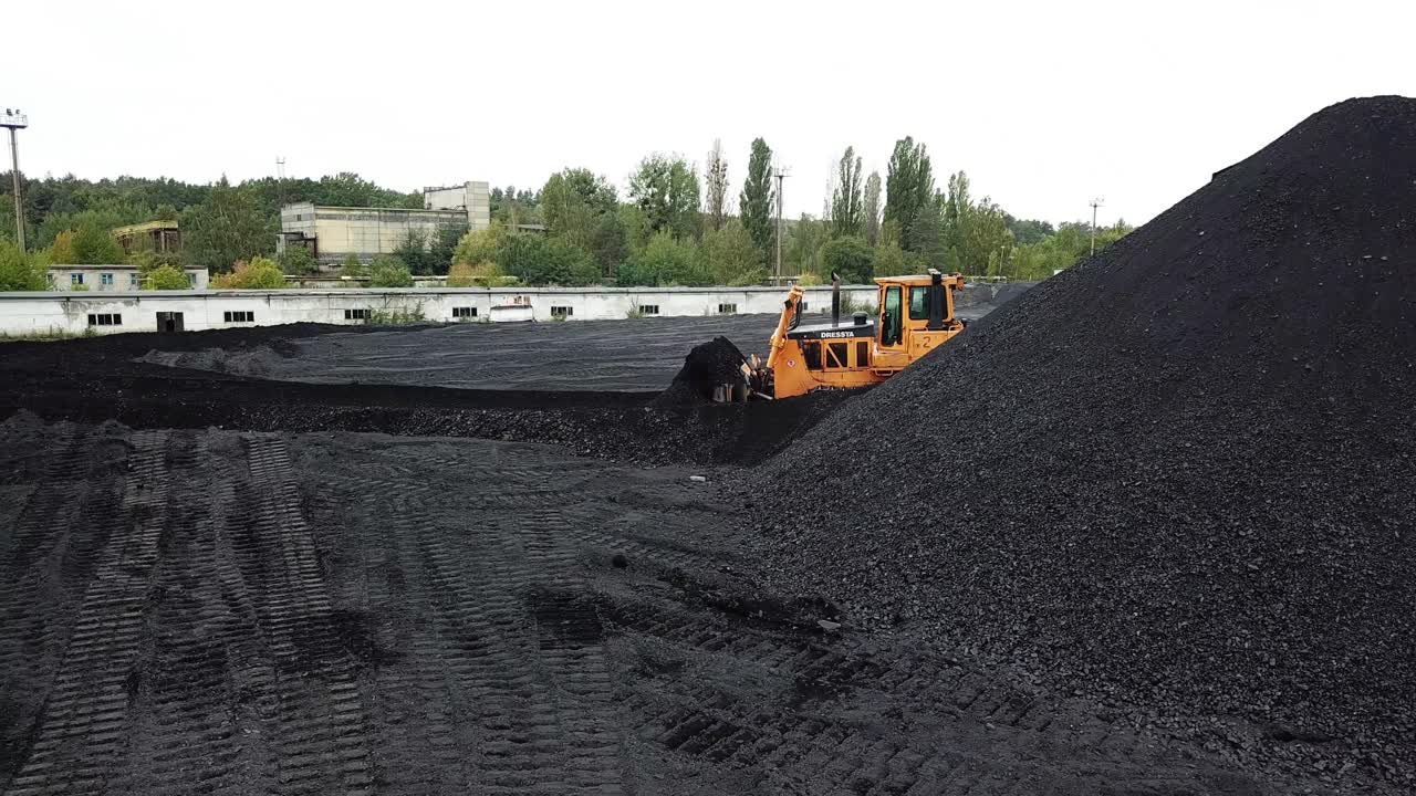Coal mining industry and transportation. Yellow tractor riding at coal warehouse for transportation