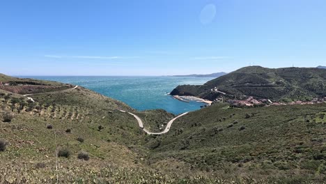 panoramic coastal view of portbou, catalonia, spain with winding roads, green hills, and the mediterranean sea under a bright blue sky
