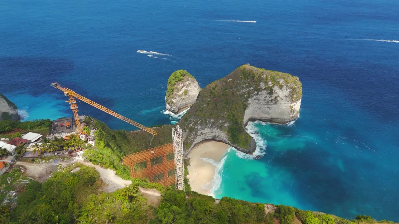 Struktur lift yang belum selesai menjulang di samping tebing T-Rex Pantai Kelingking dalam rekaman drone orbit kanan yang mulus