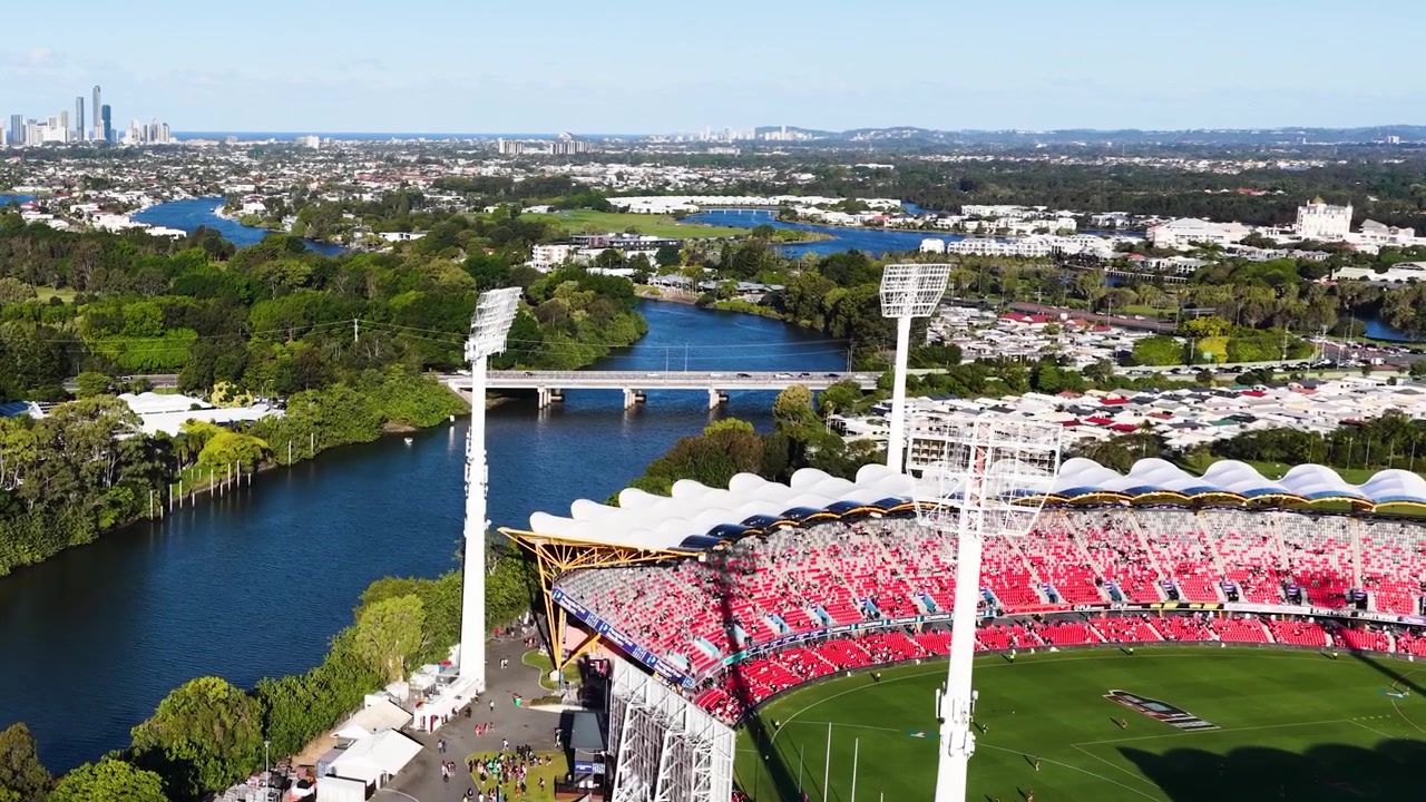 High-angle drone shot captures a crowded sports arena beside a river during bright daylight.