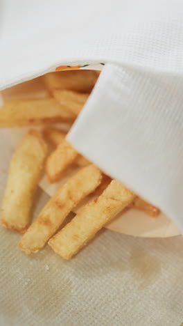 close-up of crispy golden fries partially covered with a serviette on a tray, with a hand reaching for the fries, the scene captures a relaxed and casual dining moment