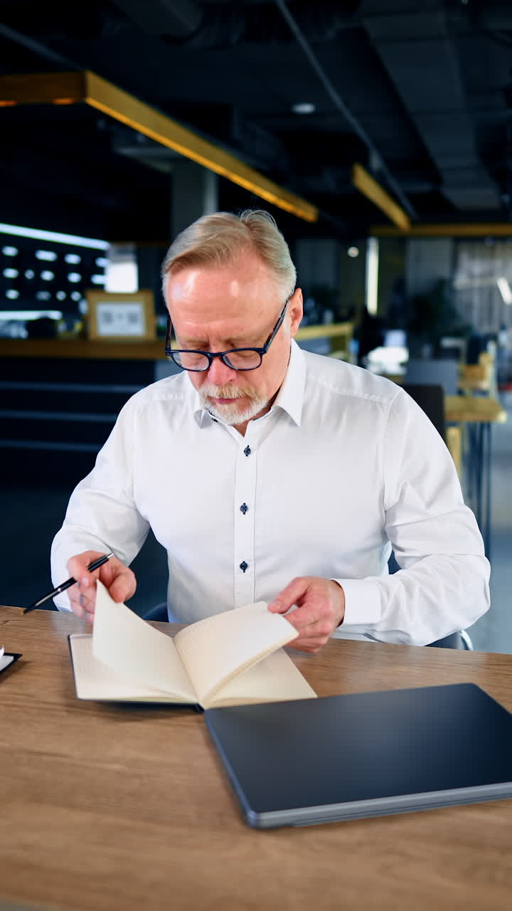 Flot, seriøs forretningsmand sidder på kontoret. Fokuseret leder på moderne arbejdsplads med bærbar computer. Vertikal video.