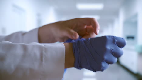 doctor putting on blue surgical gloves in hospital hallway