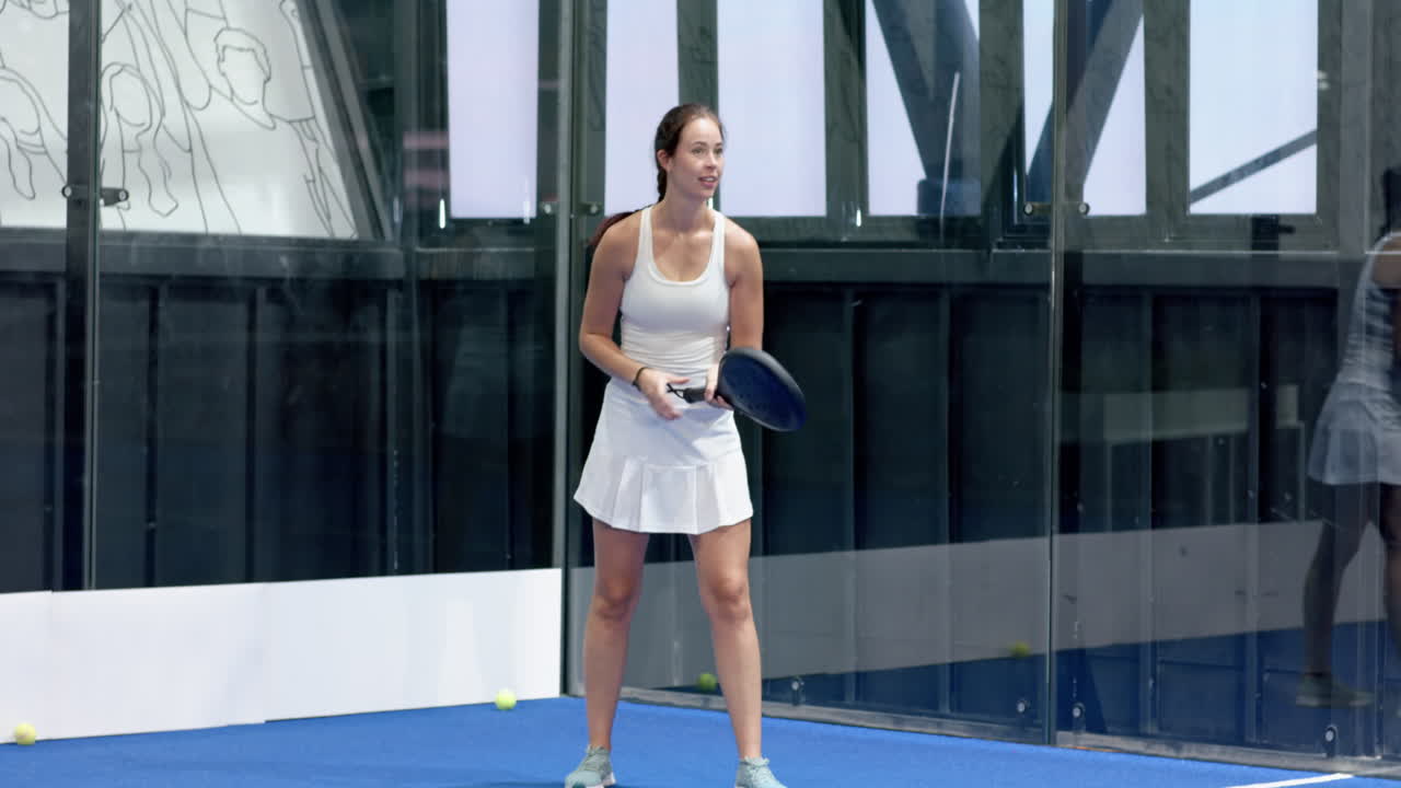Focused woman playing padel tennis on indoor court, holding racket ready to serve