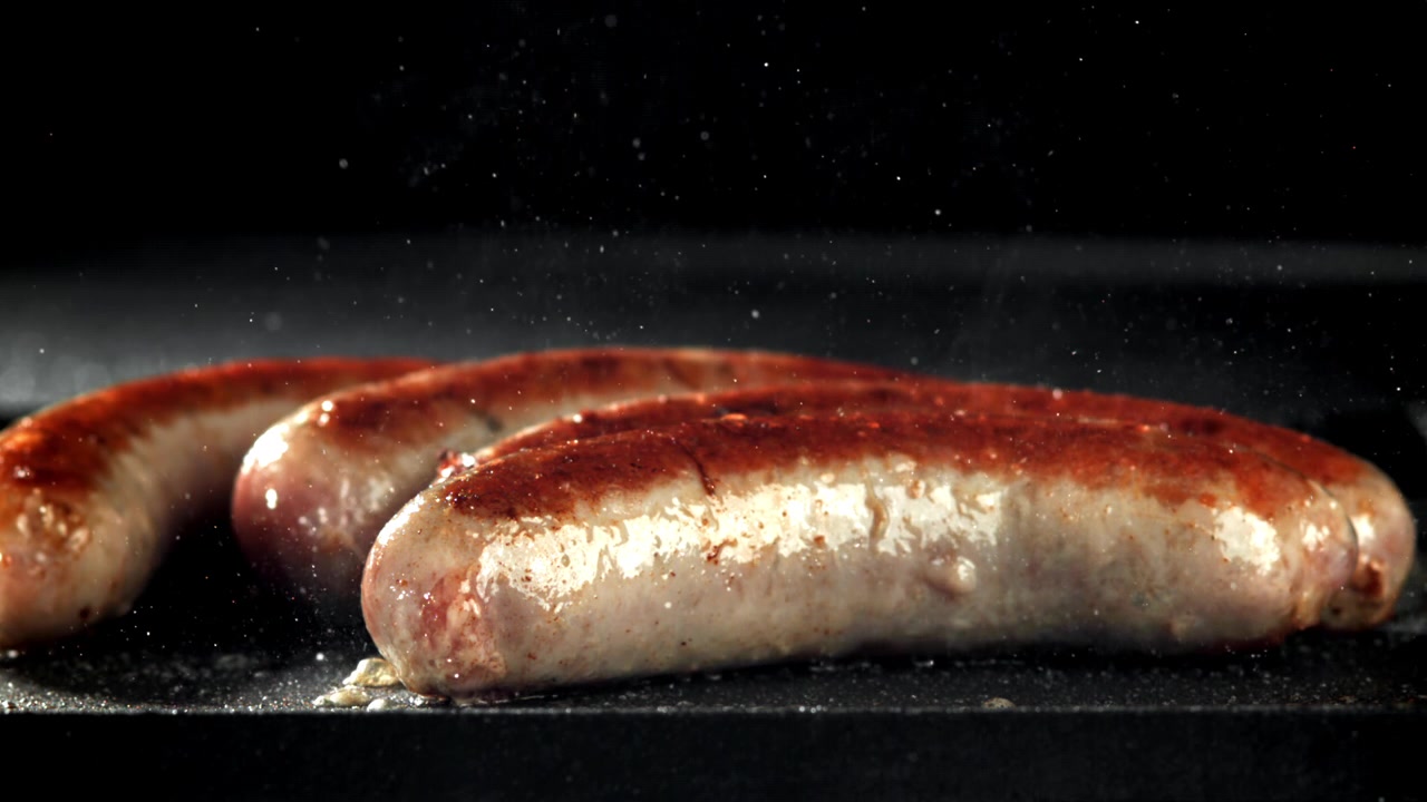 Salsicce deliziose che sfrigolano e rosolano su una griglia rovente