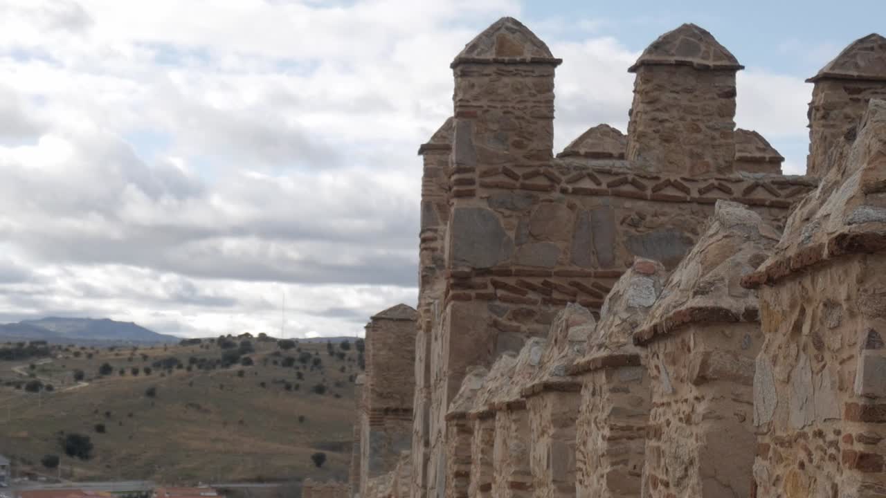 A historic stone wall with battlements in Ávila, Spain, under a cloudy sky