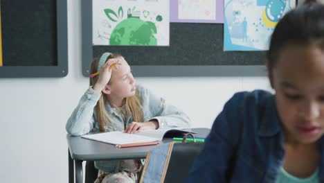 video of bored caucasian schoolgirl sitting at desk looking out of window in class, copy space