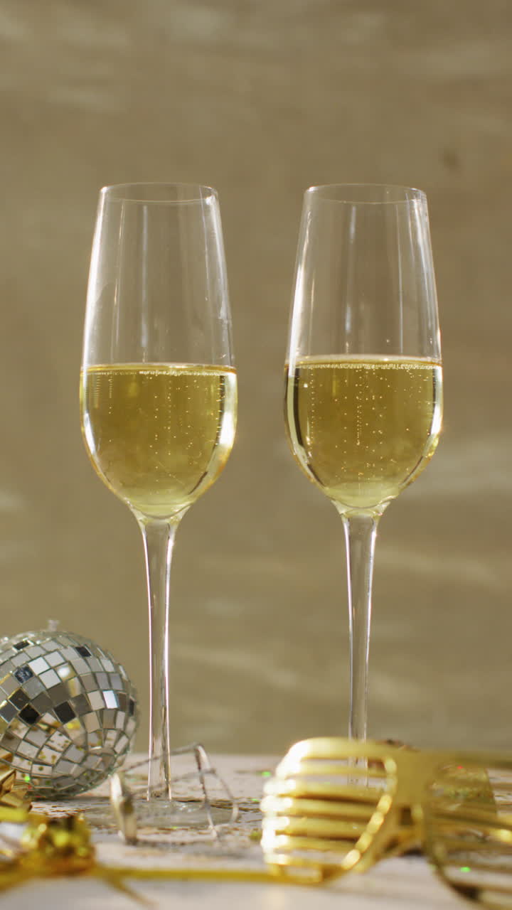 video vertical de dos vasos de champán, una mini pelota de discoteca y vasos de fiesta