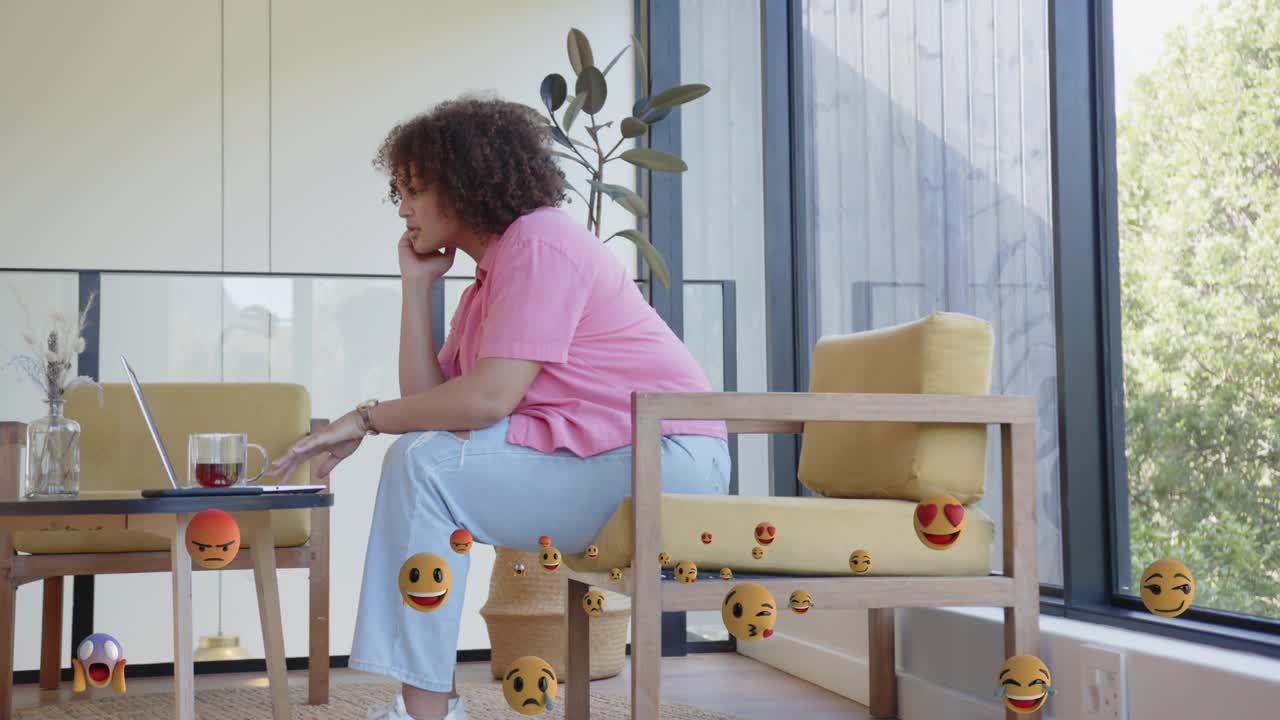Woman placing cup, typing for work on tech laptop, creating animated emoji reactions around chair