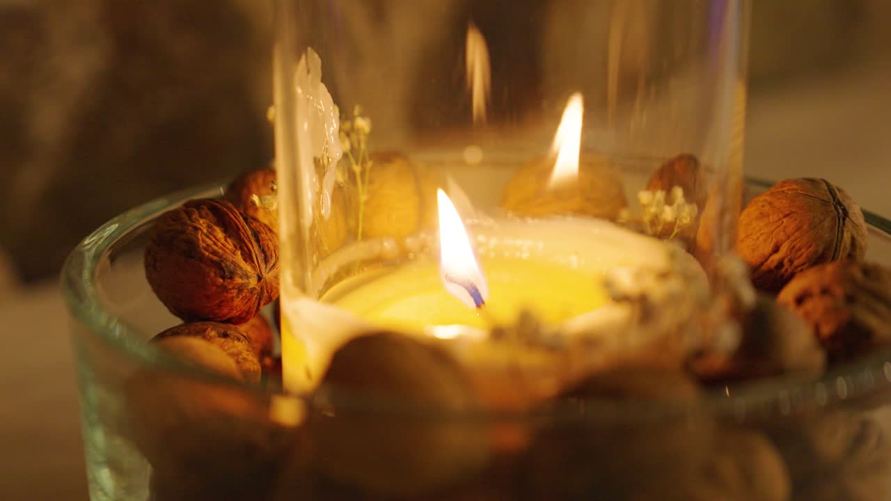 Aromatic candle burning in glass container with decorative walnuts