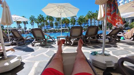 a person relaxing on a sun lounger by a pool under umbrellas, with palm trees and other loungers in the background. perfect for themes related to vacation, relaxation, summer, and resort lifestyle.