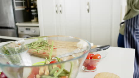 Feliz-Mujer-Mayor-Afroamericana-Preparando-Ensalada-En-Una-Cocina-Soleada,-Cámara-Lenta