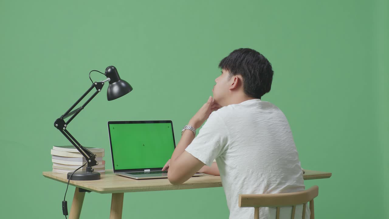 젊은 남성이 무언가에 대해 생각하고 주위를 둘러보며 집에서 녹색 화면 배경의 녹색 스크린 노트북에 타이핑하는 동안 지표손가락을 들어 올립니다.