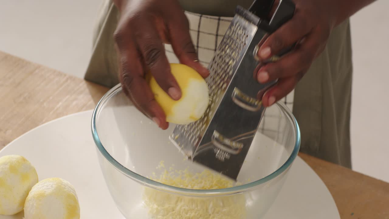 Uomo di mezza età che tiene in mano un limone sbucciato, usa una grattugia per grattugiare la scorza in una ciotola di vetro sul bancone della cucina.