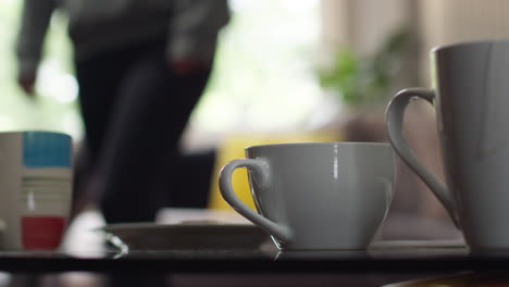 close-up von heißen getränken in tassen auf dem tisch zu hause mit snack mit person im hintergrund 1