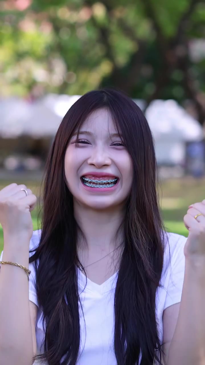 A happy young woman with dental braces cheers excitedly while smiling in an outdoor setting
