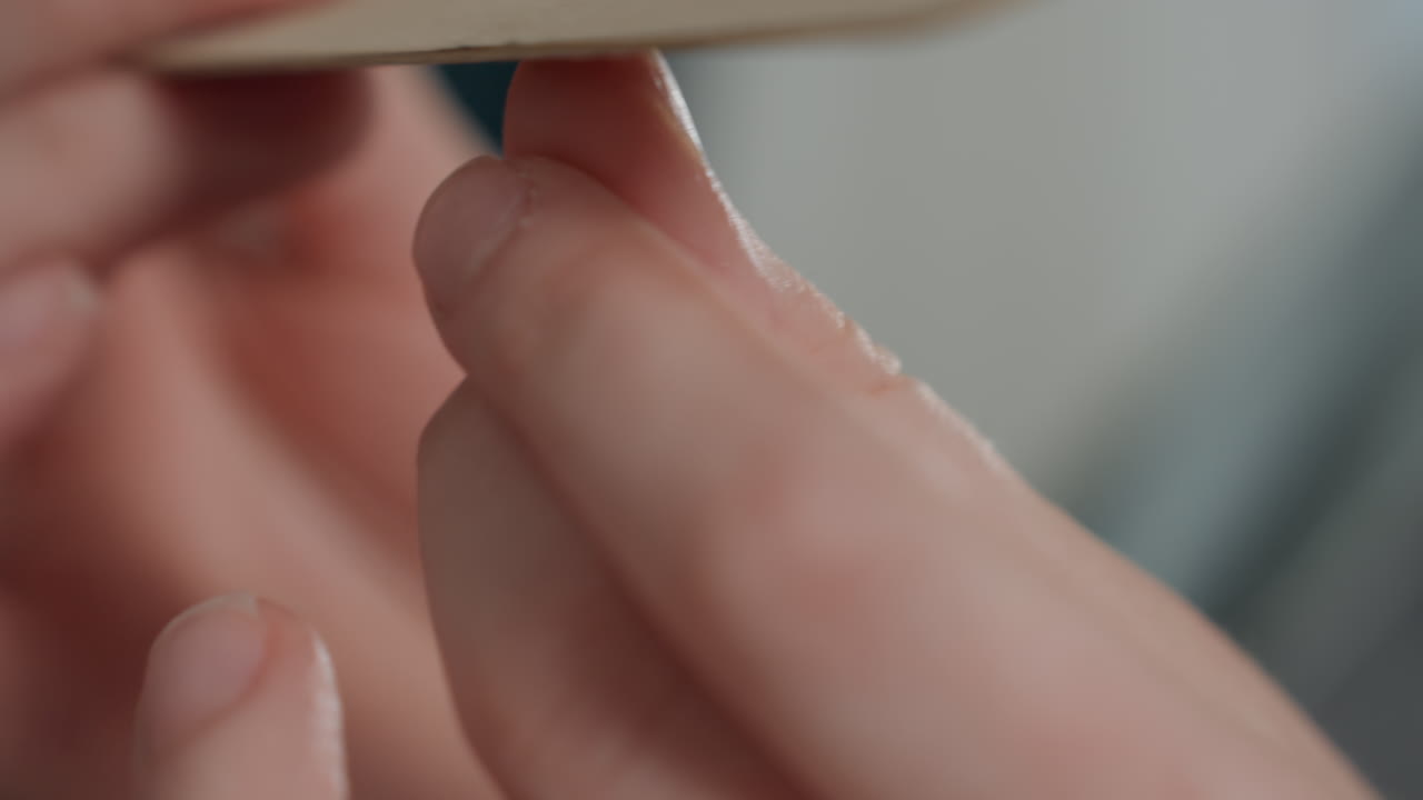 Careful hand and nail shaping. Focused shot of gentle cuticle polishing in serene setting. Intimate view of patient DIY manicure with soothing studio illumination and precise nail work