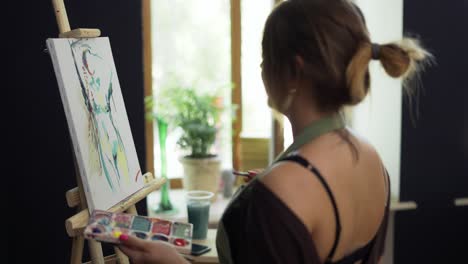 artista femenina en delantal pintando una imagen en lienzo en un estudio de arte