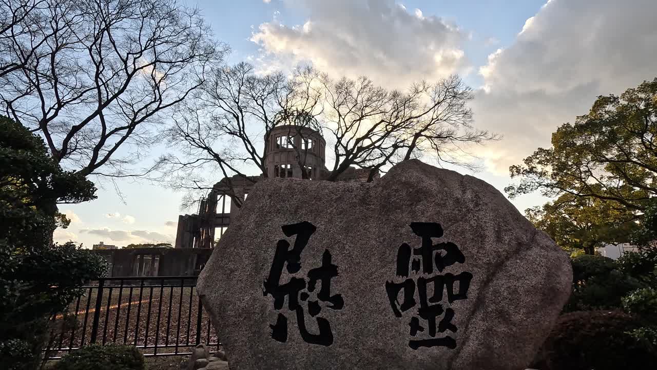 Memorial Stone and Ruins of Hiroshima Peace Dome at Sunset Framed by Bare Trees in Hiroshima Peace Memorial Park, Japan