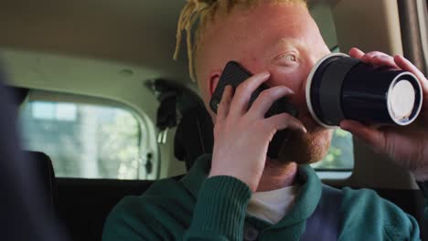 happy albino african american man with dreadlocks sitting in car talking on smartphone