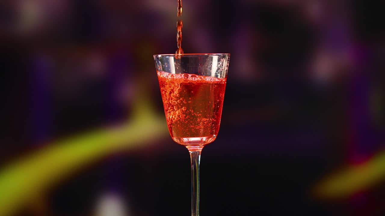 A Negroni cocktail is poured and garnished with an orange peel in a dimly lit setting