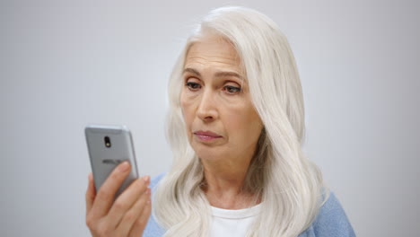 serious old woman looking cellphone indoors. senior lady searching news inside.