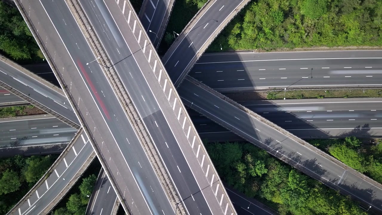 Aerial timelapse captures dynamic traffic flow through a complex highway interchange. Vehicles navigate multiple levels of connecting motorways.