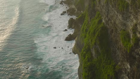 rock cliffs with large swell waves crashing onto shore during sunset, nusa penida, aerial