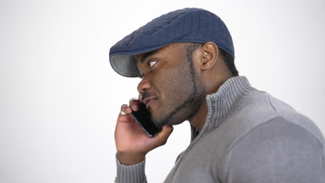 facial portrait of african man with a phone. young guy with black skin in stylish blue cap talking on the mobile phone on white background. profile view.
