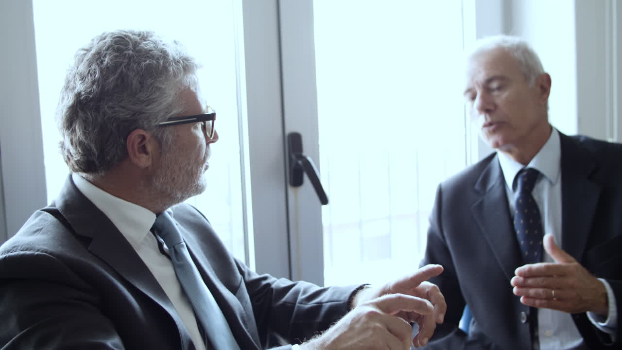 직장에 앉아 있는 두 명의 진지한 회색 머리 임원