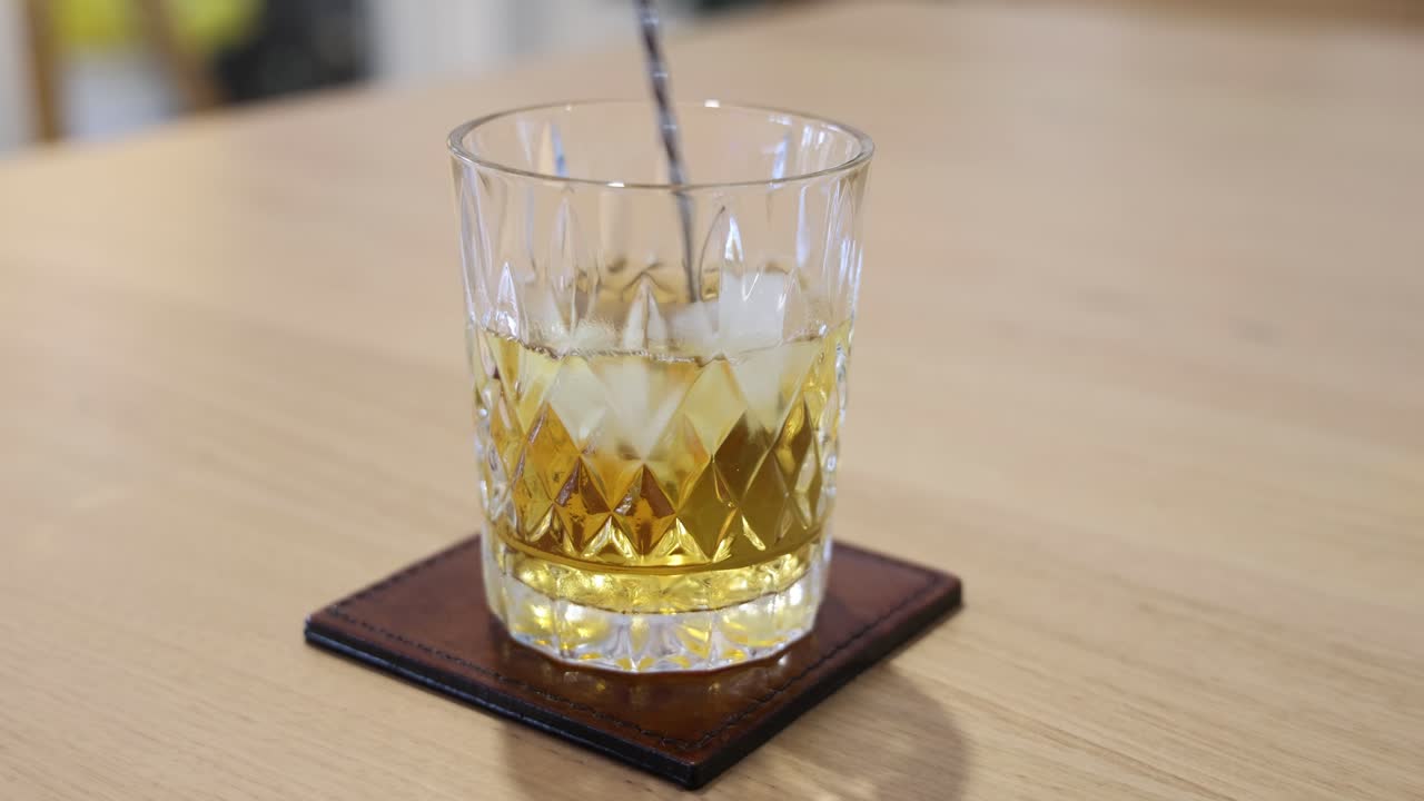 una cuchara agita cubos de hielo en un vaso de whisky