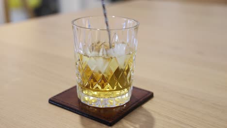 a spoon stirs ice cubes in a whiskey glass