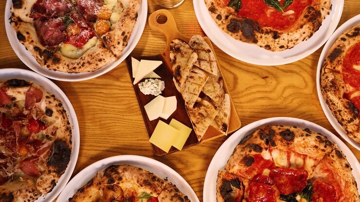 Vista dall'alto di varie pizze, formaggio e vino su un tavolo di legno durante la cena