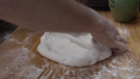Close-up-on-chef-hands-forming-the-pizza-dough-on-a-wooden-table