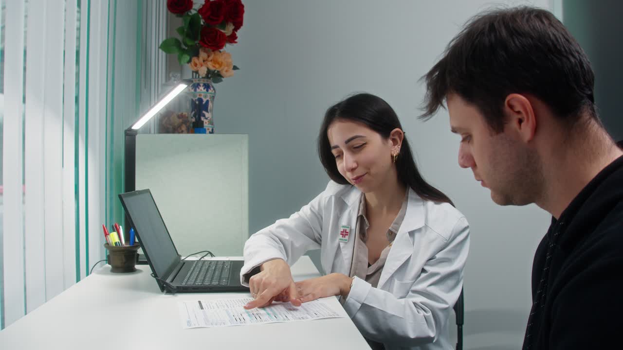 Ahli gizi wanita meninjau rencana diet dengan pasien pria selama konsultasi klinik, terekam dengan gerakan kamera "push in" yang halus di latar kantor modern