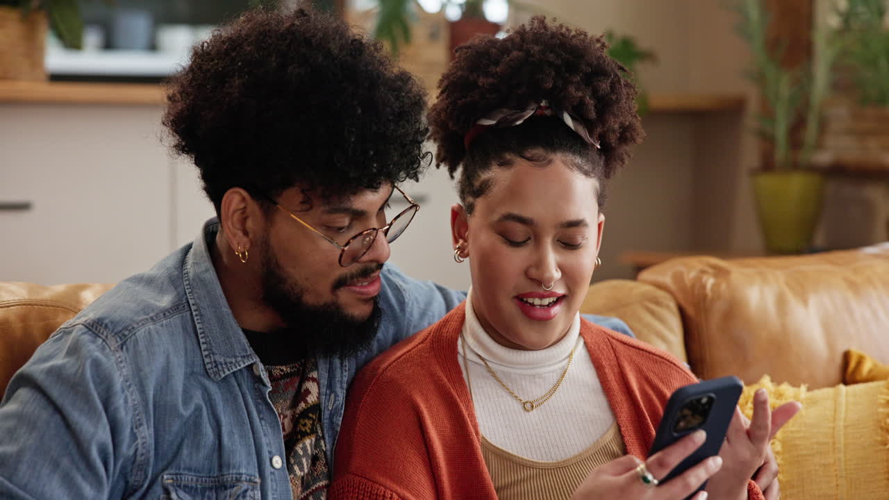 una pareja acurrucada en un sofá mientras miran su teléfono.