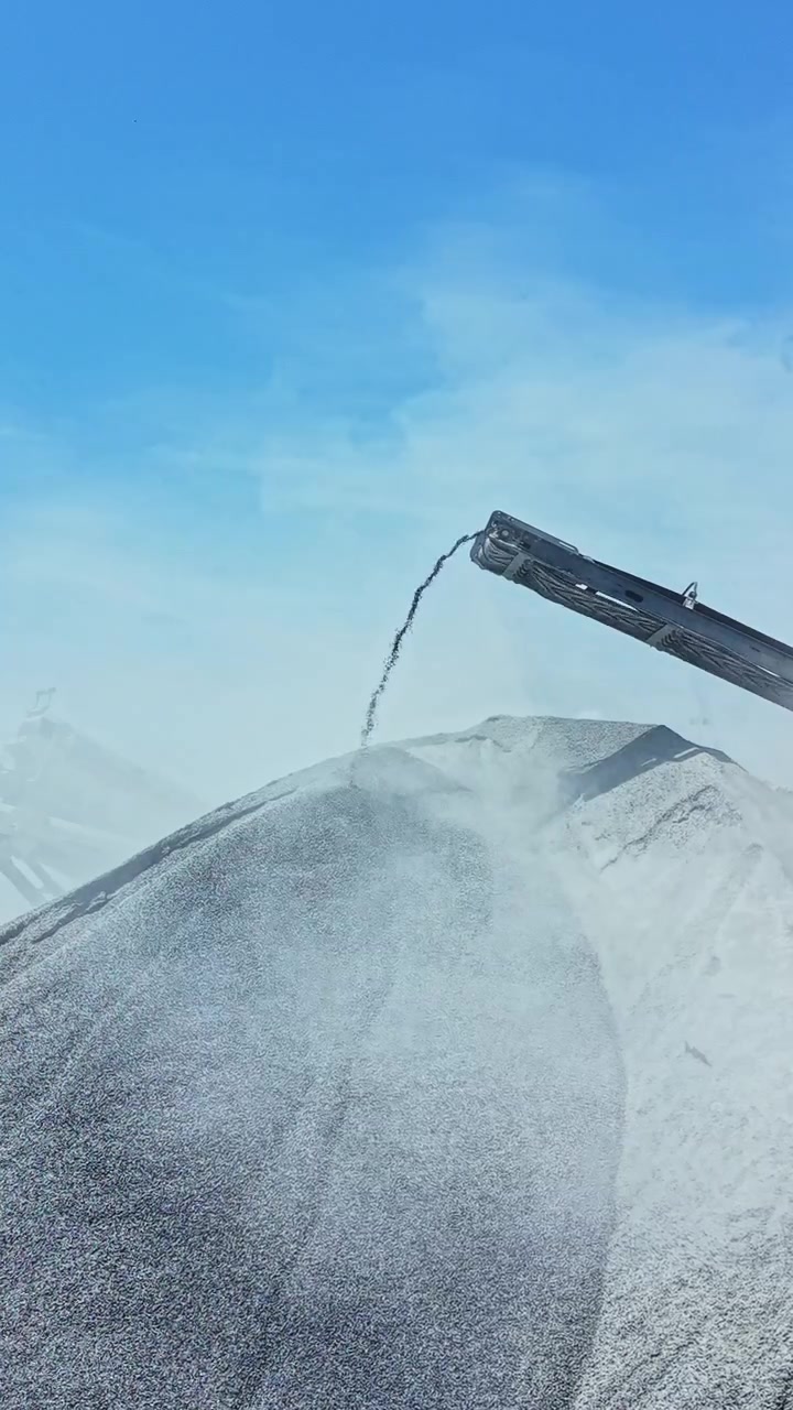 Granite quarry operation shows equipment pouring granite material on a stockpile under a clear blue sky in the afternoon