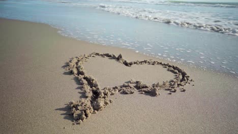 el dibujo en forma de corazón en la arena de la playa está siendo parcialmente arrastrado por una ola marina