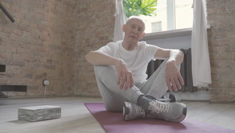 old male sitting on yoga mat at home