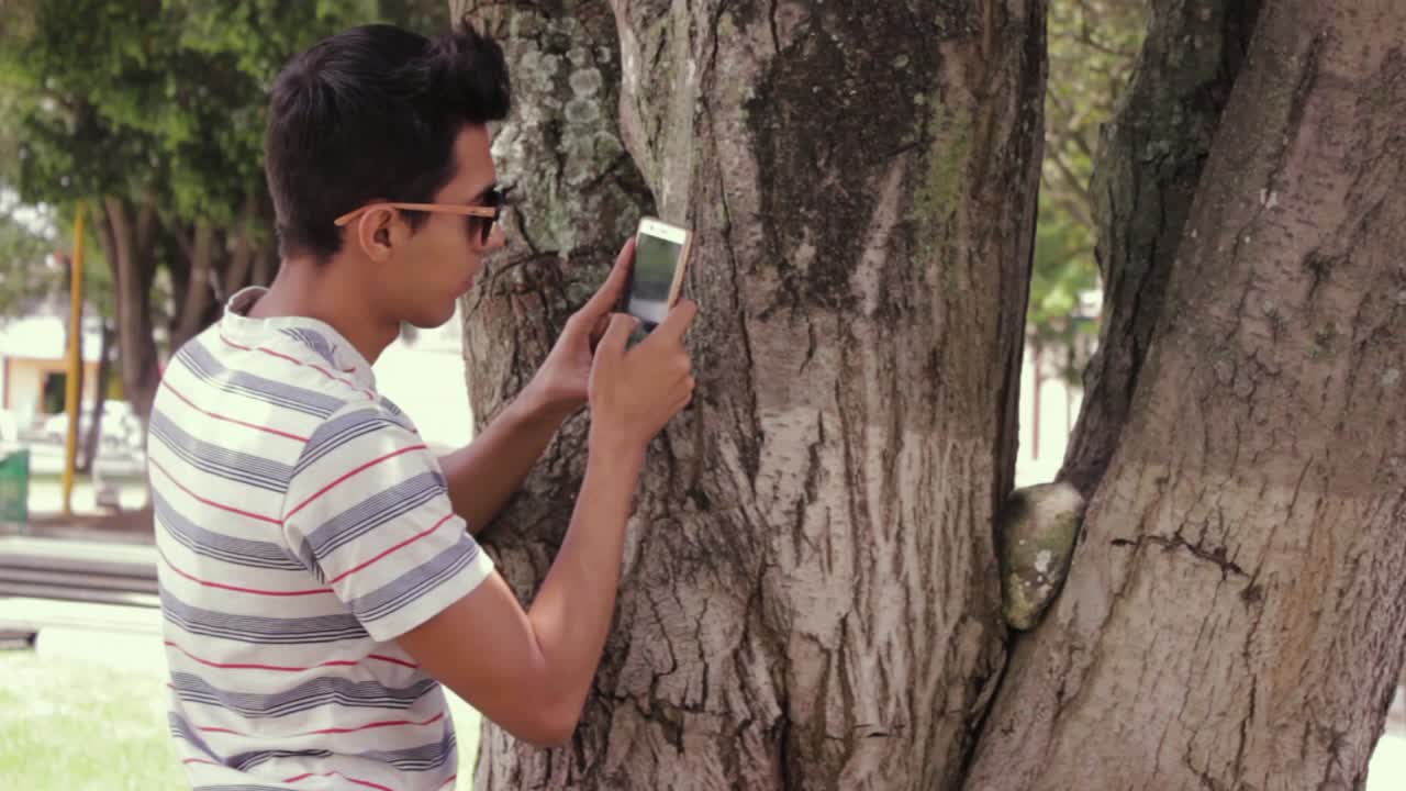 joven en el parque usando su celular para tomar fotos y videos de la naturaleza