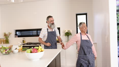 senior couple dancing in kitchen wearing aprons, enjoying time together