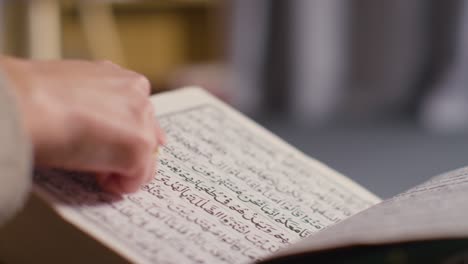 close up of person turning pages of the quran on stand at home