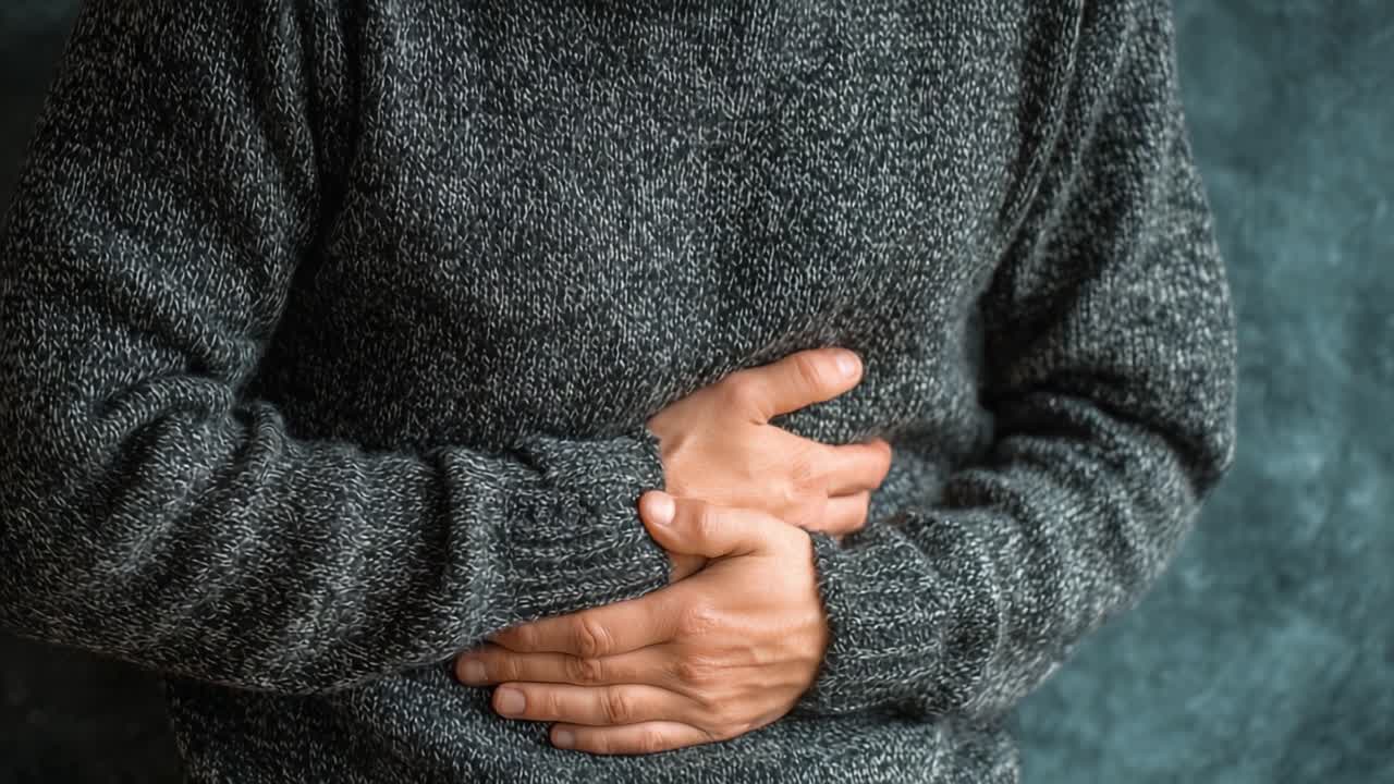 A Person Grasping Their Abdomen in Discomfort, Wearing a Gray Sweater, Perhaps Experiencing Digestive Issues or Stomach Pain, Set Against a Textured Background