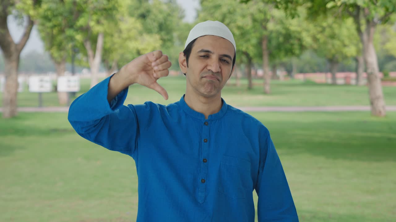 실망 한 무슬림 남자 가 공원 에서 엄지손가락 을 내려놓고 있다