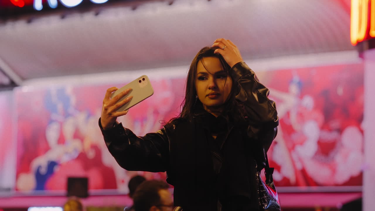 Young woman taking a selfie in front of the Moulin Rouge building, in Paris, France, at night