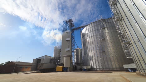 industrial plant in the countryside. modern agricultural complex with storage bins to process grains. white vapor over the industrial equipment. grain elevators for storing.