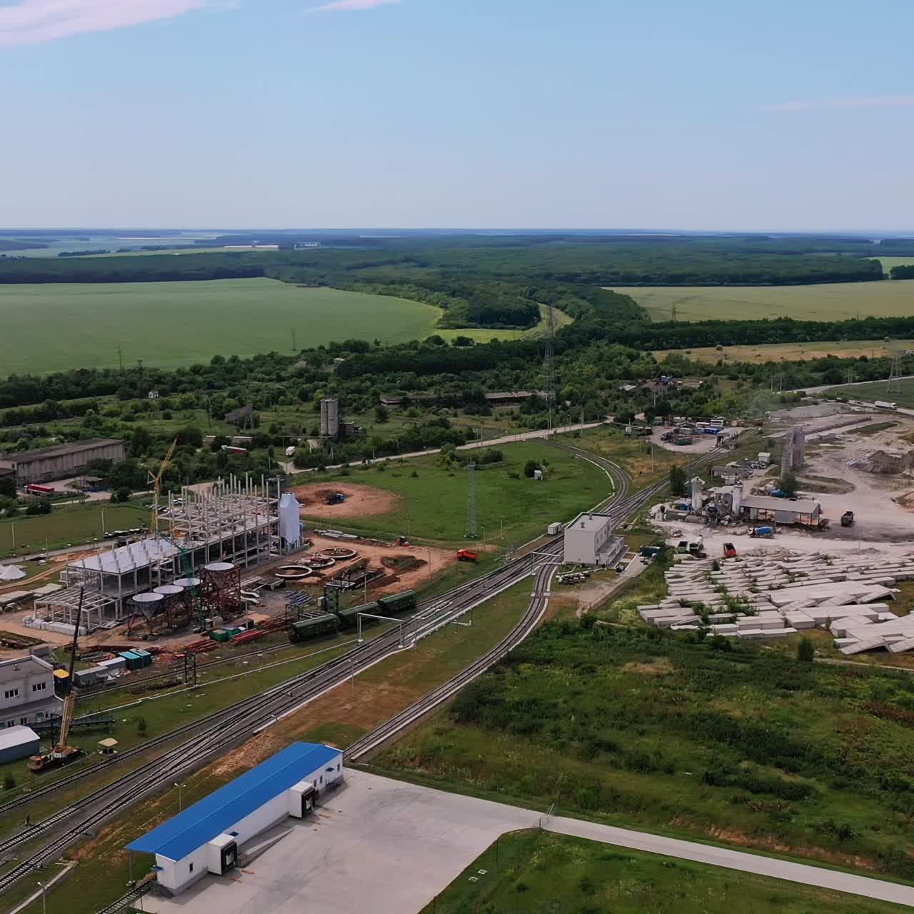 New premises being constructed for modern granary plant. Railways with cargo trains near the construction site. Beautiful farmlands at the background