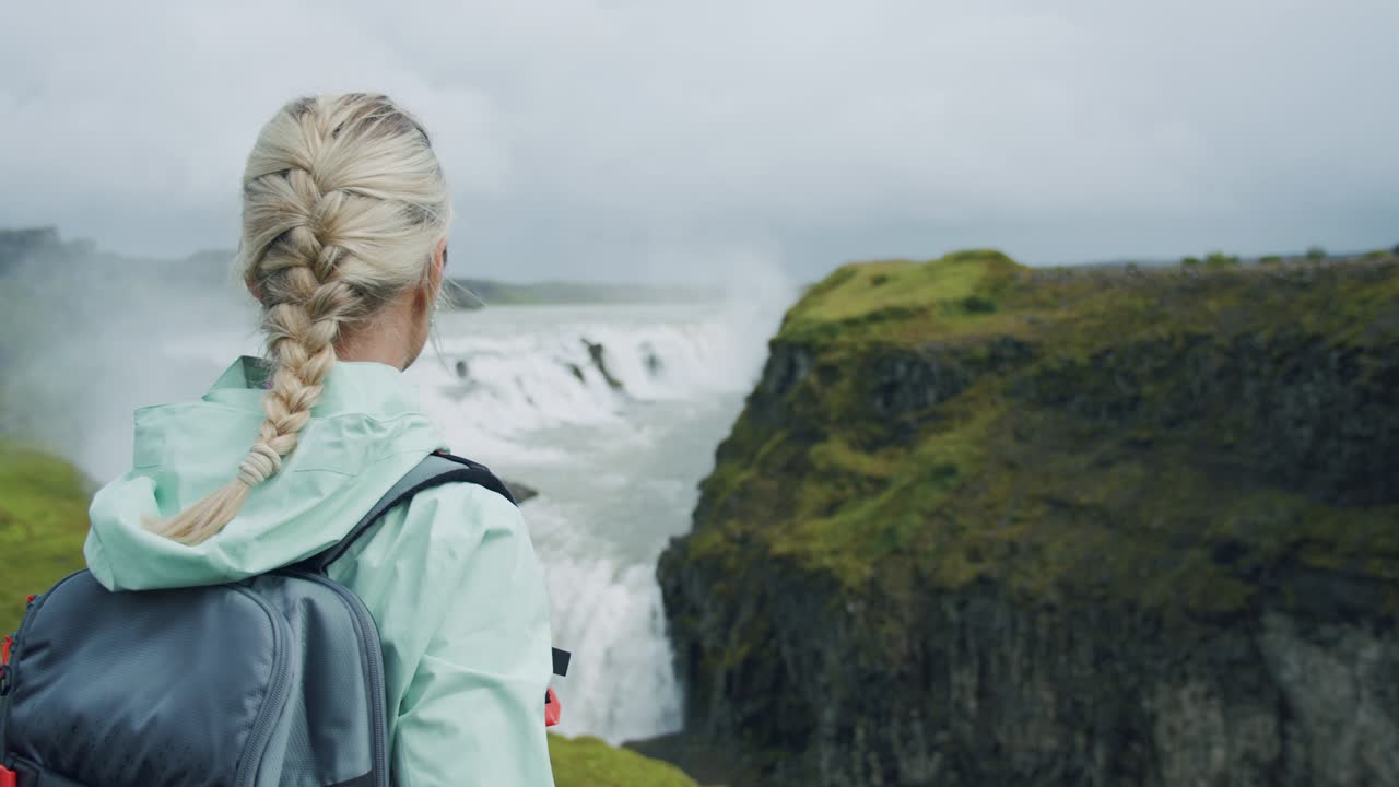 vista trasera de una mujer viajera con mochila disfrutando de la cascada de gullfoss, famosa atracción turística y destino histórico en islandia en el círculo dorado
