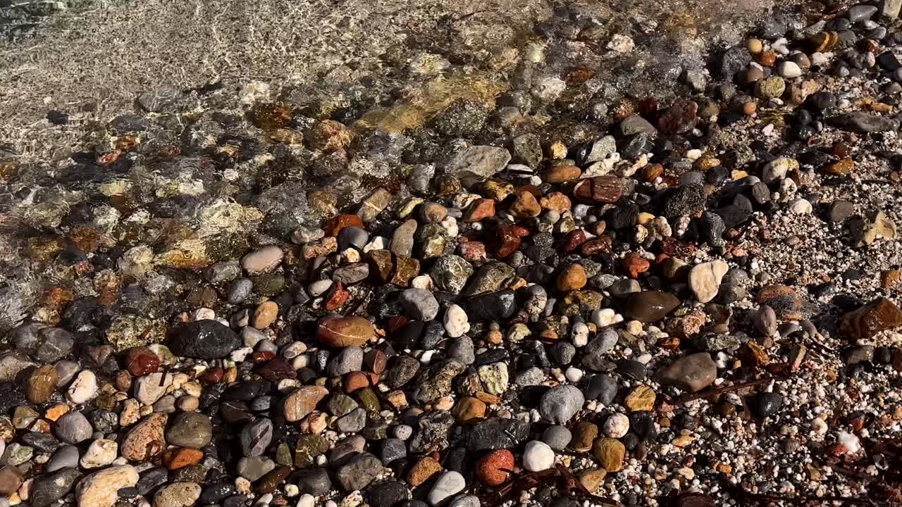 Close up of a rocky beach with wet pebbles and shallow water in Crete Greece