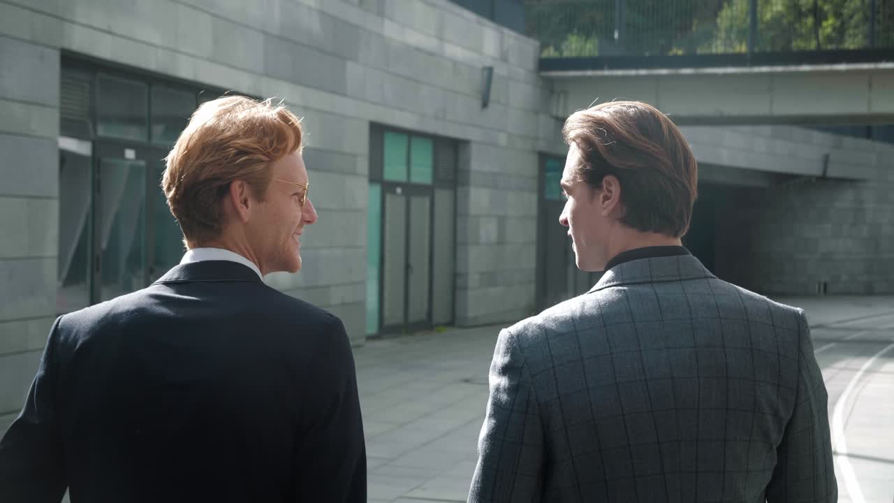 vista trasera de dos hombres de negocios discutiendo acuerdos mientras caminan fuera de la oficina en el descanso. hombres inversores financieros están hablando al aire libre. dos colegas se comunican en el camino al trabajo